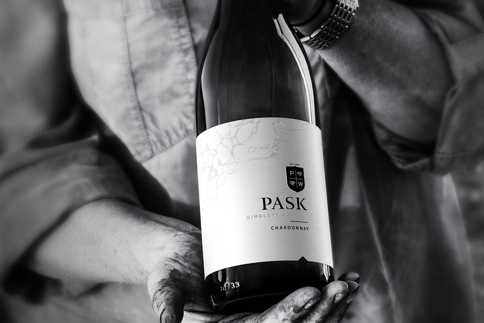 Hands holding a bottle of Pask Gimblett Chardonnay, black and white close-up shot