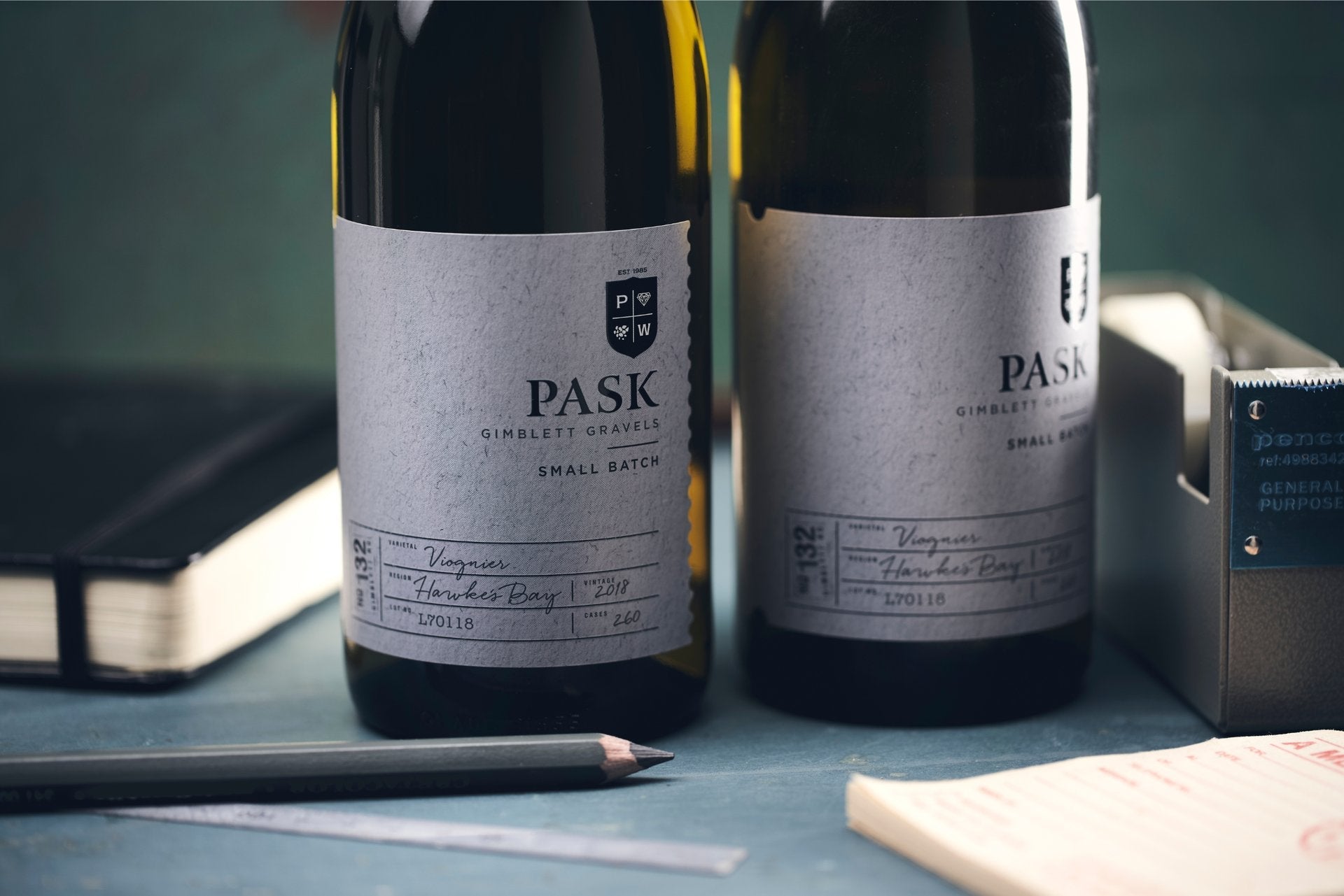 Two Pask Gimblett Gravels Small Batch Viognier bottles on a desk beside a pencil and notepad