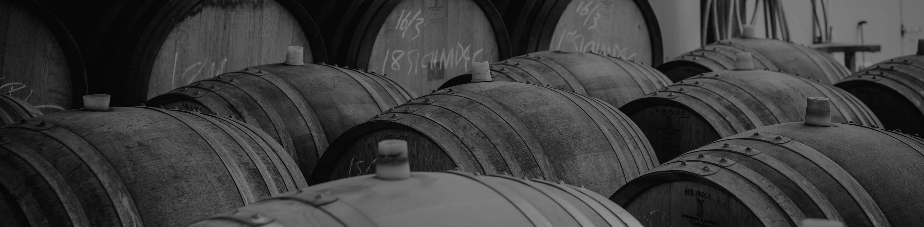 Black and white image of oak wine barrels with vintage chalk markings stacked in the Pask Winery cellar