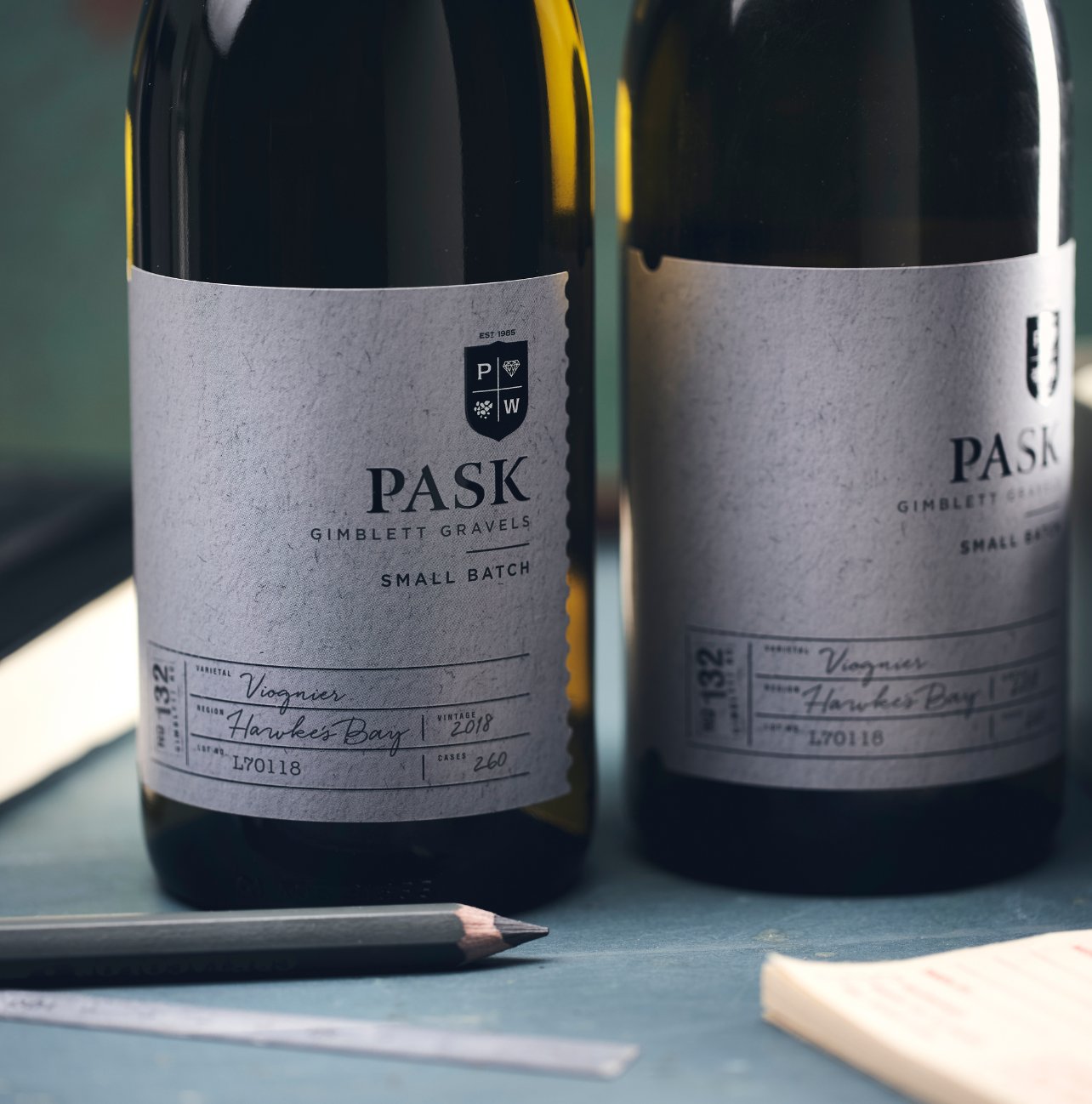 Two bottles of Pask Gimblett Gravels Small Batch Viognier, Hawke's Bay, resting on a surface beside a pencil.