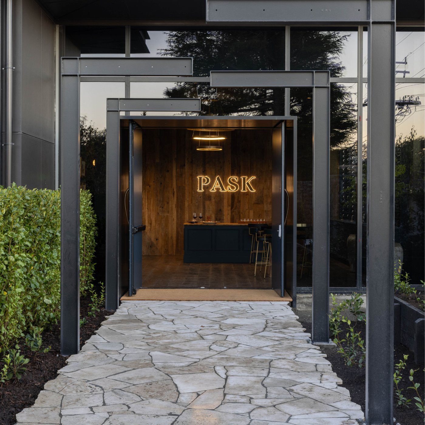 Pask Winery cellar door entrance with illuminated PASK sign, stone pathway, and dark timber interior visible through open glass doors